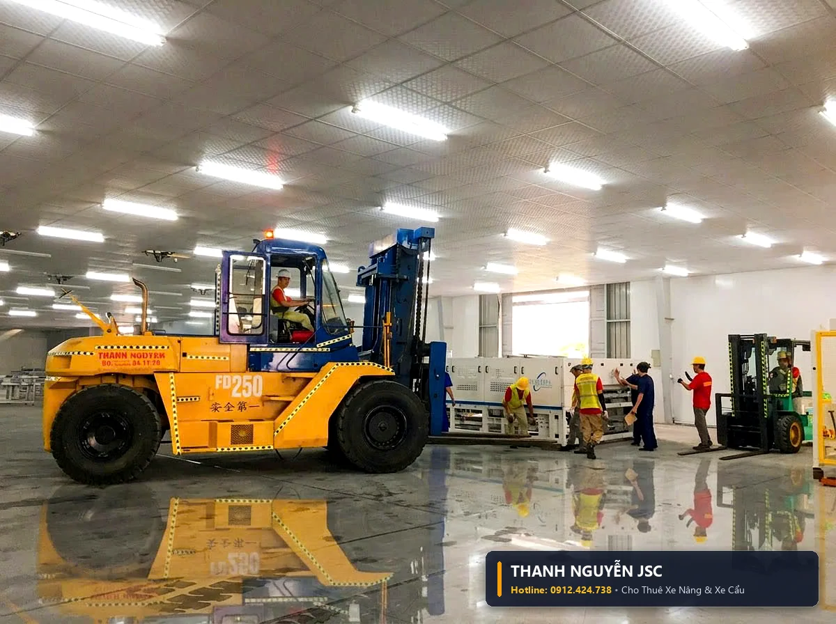 Hai xe nâng trọng tải lớn đón nhận các kiện máy móc hạ tải từ xe container ngoài cửa xưởng