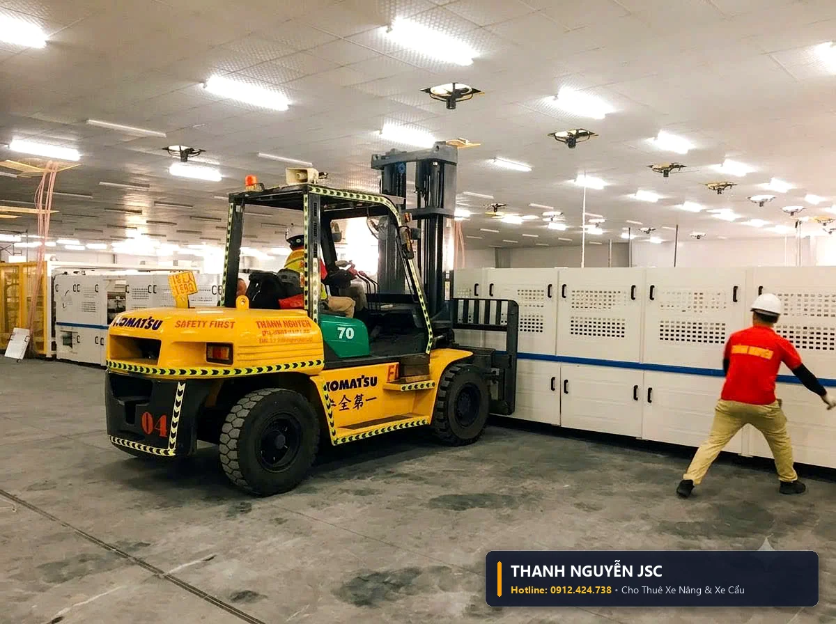 Xe nâng hàng Komatsu màu vàng nâng hạ khối máy móc trắng tinh khôi trong phòng sạch nhà máy điện tử